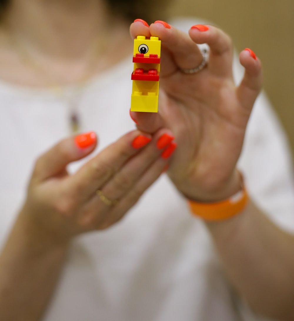 Mãos segurando um pequeno pato de LEGO construído com poucas peças