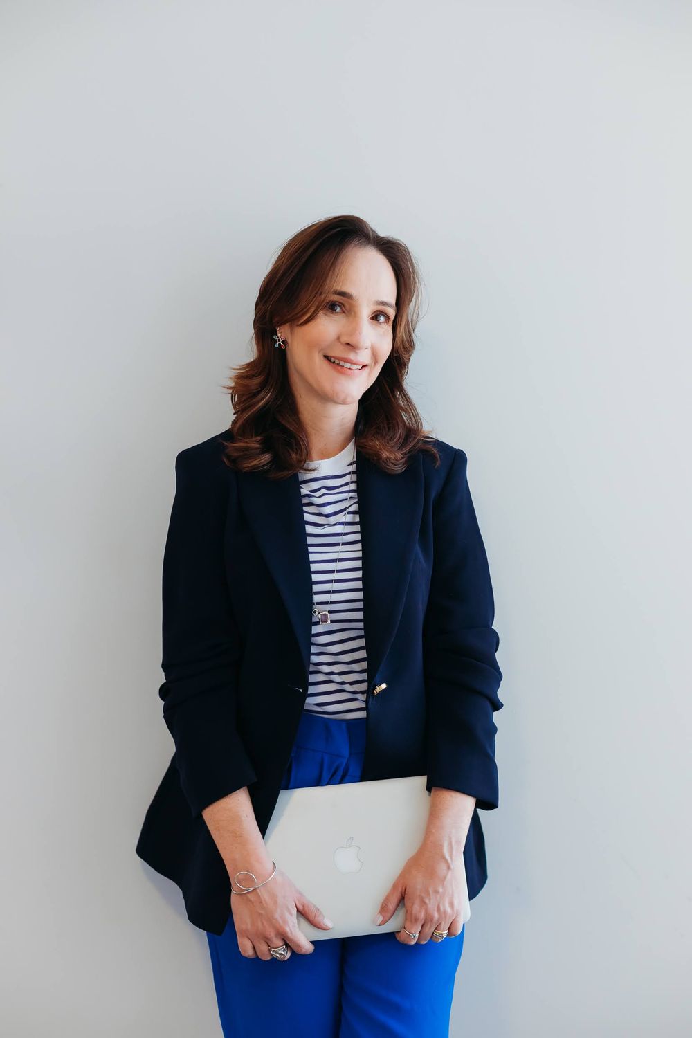 Retrato de Natália Longhi, de blazer azul, segurando um notebook