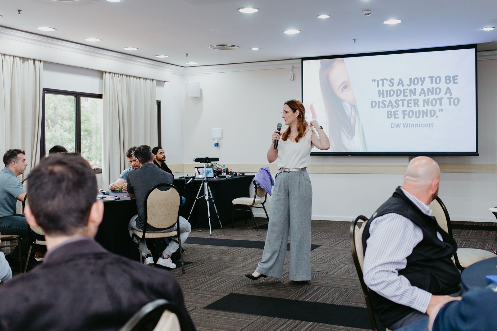 Natália falando a um grupo de líderes, com uma frase de Winnicott projetada na tela